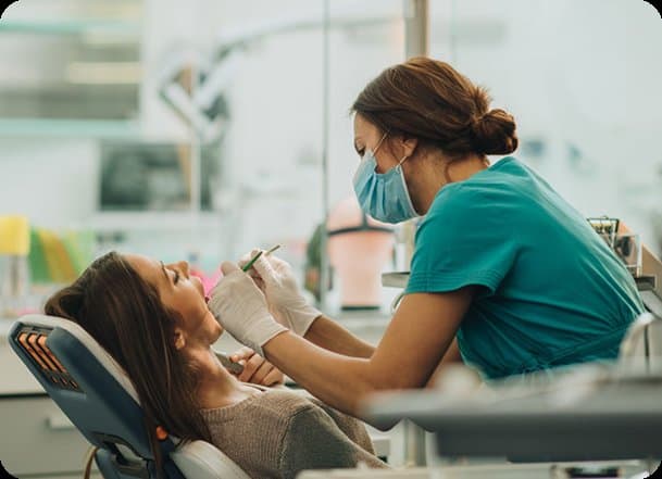 A dentist in teal scrubs treating a patient in the surgery